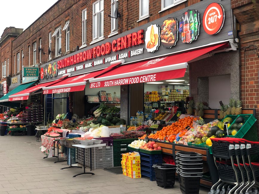 A vibrant outdoor display of fresh flowers arranged in bouquets and floral arrangements, situated on tables and crates in front of South Harrow Food Centre. The flowers include bright red and yellow r