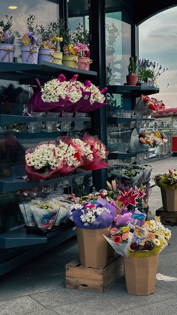 A display of fresh floral arrangements at a florist shop, featuring vibrant bouquets of white, pink, purple, and yellow flowers. The arrangements include chrysanthemums, lilies, and other seasonal blo