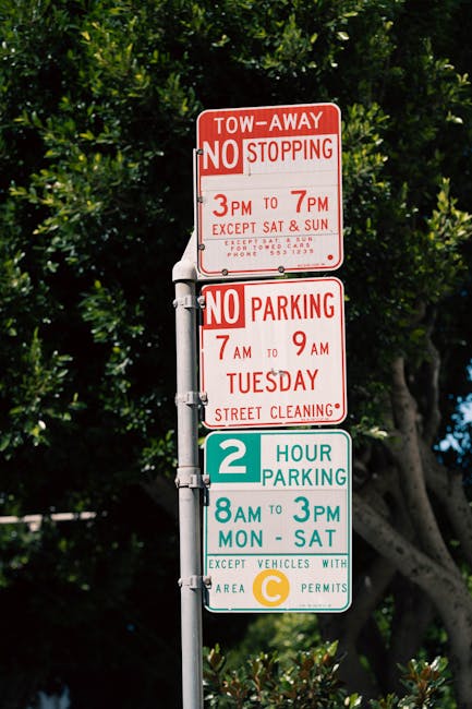 The image shows a set of three parking and traffic restriction signs mounted on a metal pole in an outdoor setting with lush green trees in the background. The top sign, in red and white, indicates a 