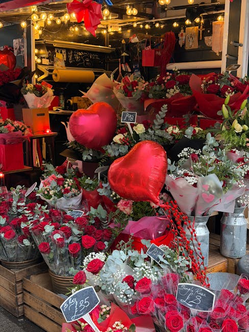A display of various floral arrangements and gift items at a flower shop, featuring red and white roses, greenery, and heart-shaped balloons. The arrangements are wrapped in decorative paper and place